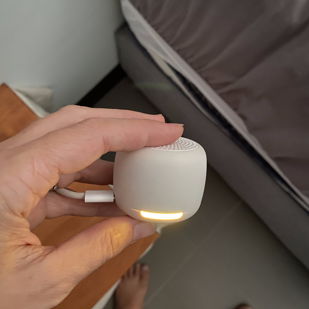 Babelio portable white noise machine with warm night light held in hand beside a bed