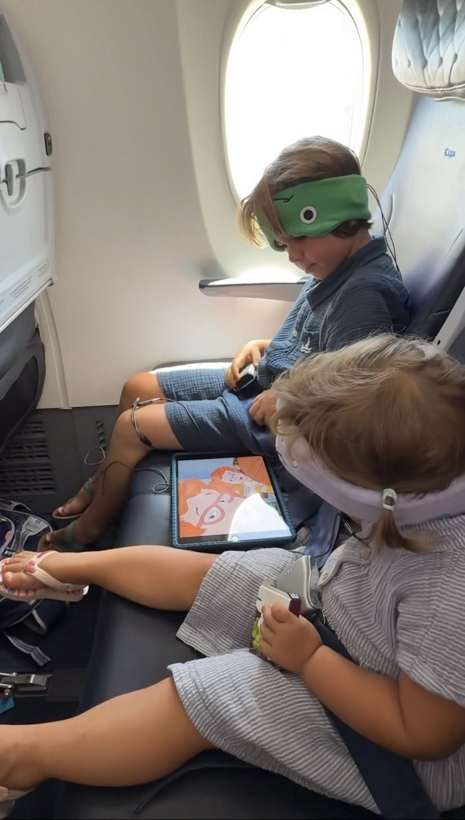 Two kids wearing CozyPhones headphones watching a tablet on a plane